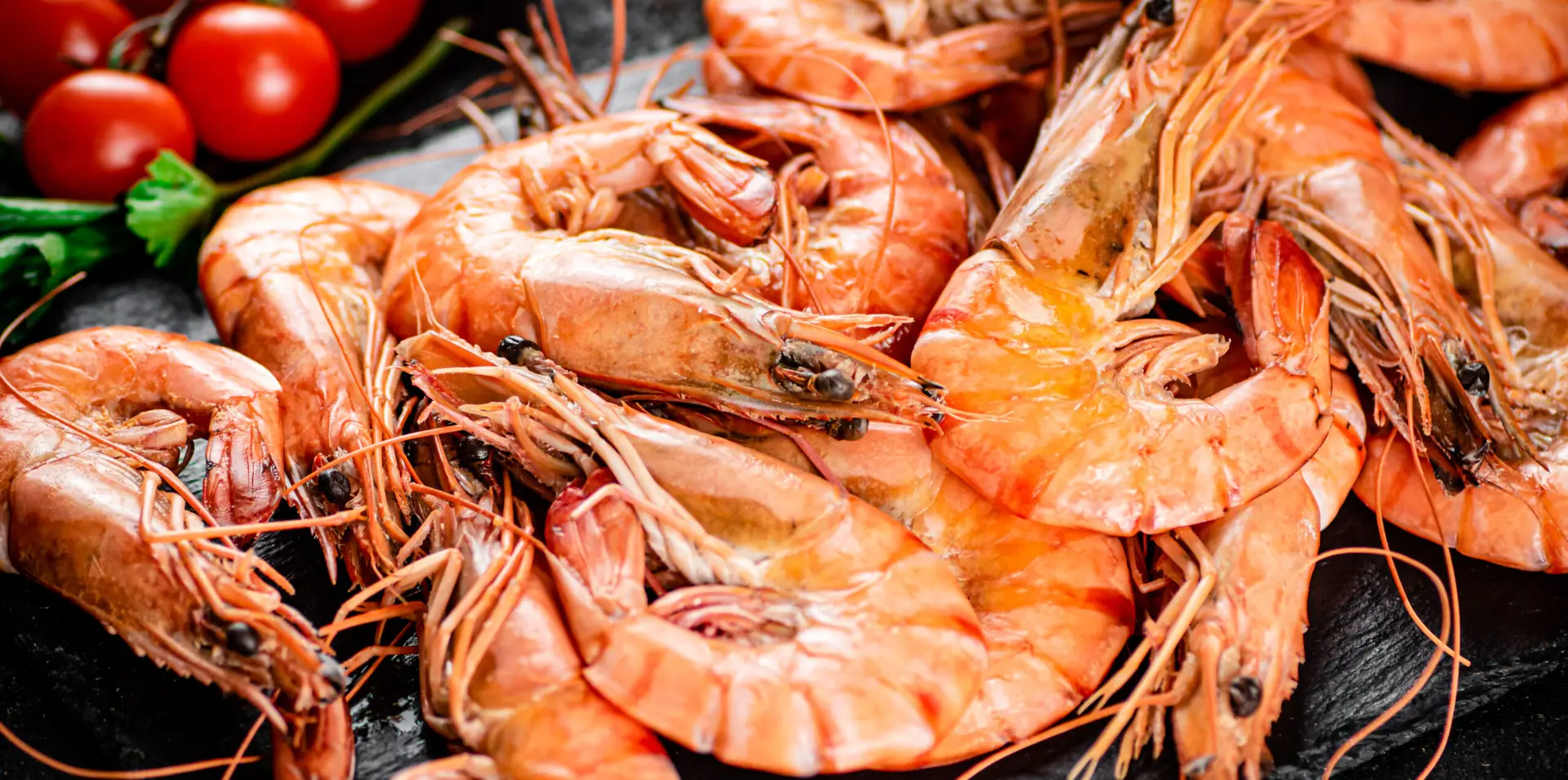 Boiled shrimp on a stone board with tomatoes and parsley.